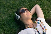 Young woman lying on grass, wearing headphones and sunglasses